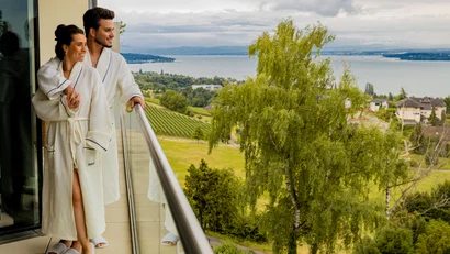 Paar in Bademänteln auf Balkon mit Blick auf See und bewölkten Himmel