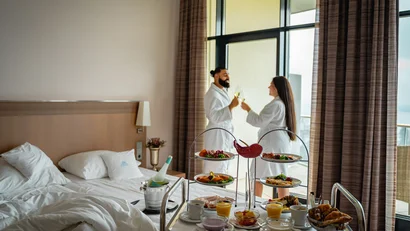Paar im Bademantel stoßt mit Champagner in Hotelzimmer mit Frühstück an