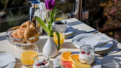 Tisch mit Frühstück, Blumen, Brötchen, Obst, Joghurt und Getränken im Freien
