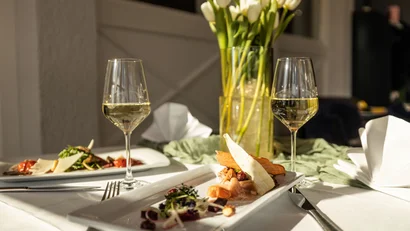 Weißer Tulpenstrauß und zwei Sektgläser auf einem gedeckten Tisch mit Vorspeisen
