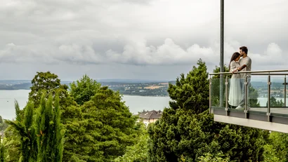 Paar umarmt sich auf Balkon mit Blick auf bewölkten Himmel und Landschaft
