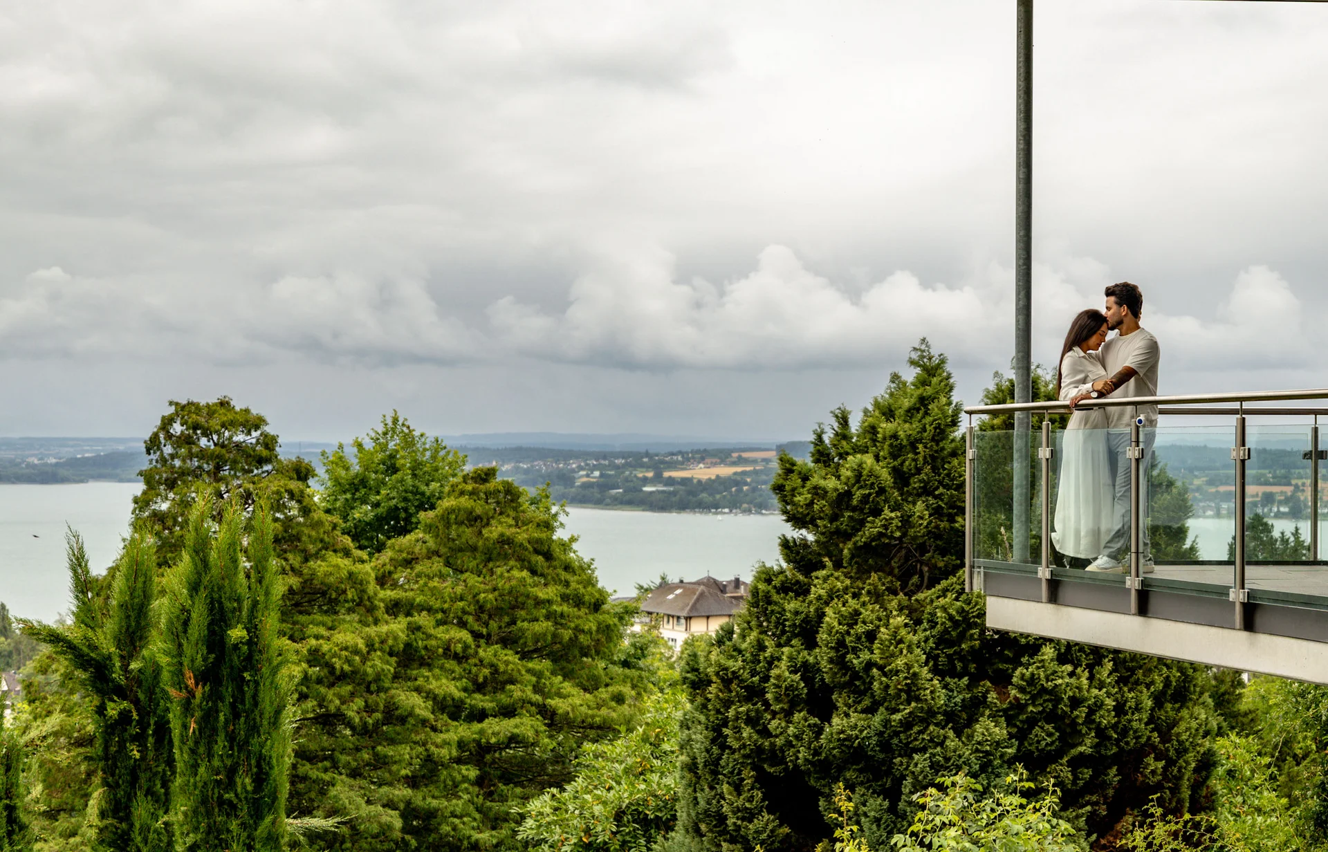 Paar umarmt sich auf Balkon mit Blick auf bewölkten Himmel und Landschaft