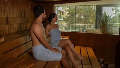 Zwei Personen entspannen gemeinsam in einer hölzernen Sauna mit Blick nach draußen