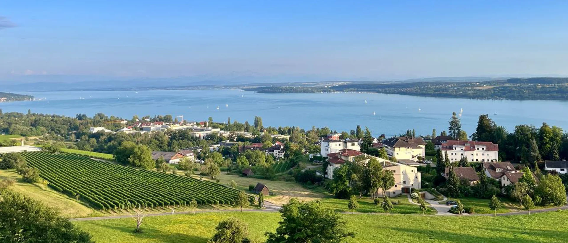 Blick auf Dorf, grüne Felder und See unter blauem Himmel mit Wolken
