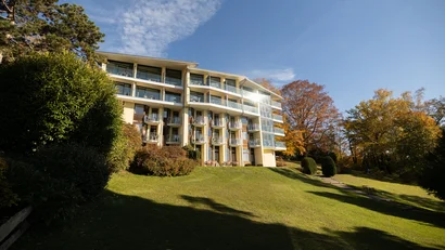 Modernes Appartementhaus mit Glasbalkonen und Herbstbäumen bei blauem Himmel