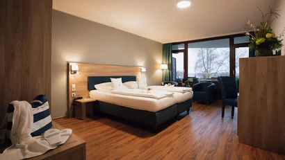 Gemütliches Hotelzimmer mit Doppelbett, Sesseln und großem Fenster mit Ausblick