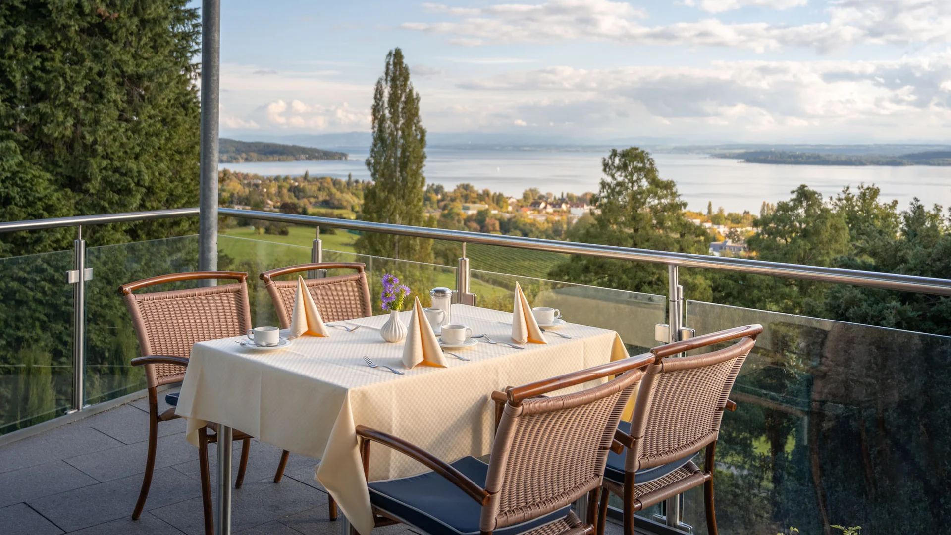 Terrasse mit gedecktem Tisch und Blick auf See und bewaldete Hügel