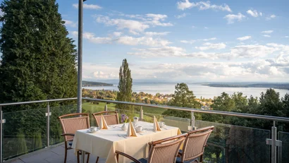 Terrasse mit gedecktem Tisch und Blick auf See und bewaldete Hügel